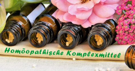 Homöopathische Komplexmittel sind Tausendsassas. Zur Verbildlichung, dass hier mehrere Einzelmittel zusammengefasst wirken, liegen mehrere Globuliflschchen geöffnet nebeneinander unter Blüten auf einem Tuch