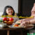 Geniessen ist Lebenskunst - Prof Grönemeyer sagt man solle nichts essen, das die Großmutter nicht als Essen erkannt hätte. Im Bild bereitet eine Oma im Anschnitt an einem Tisch mit Apfelschale Essen für ein lächelndes Mädchen zu